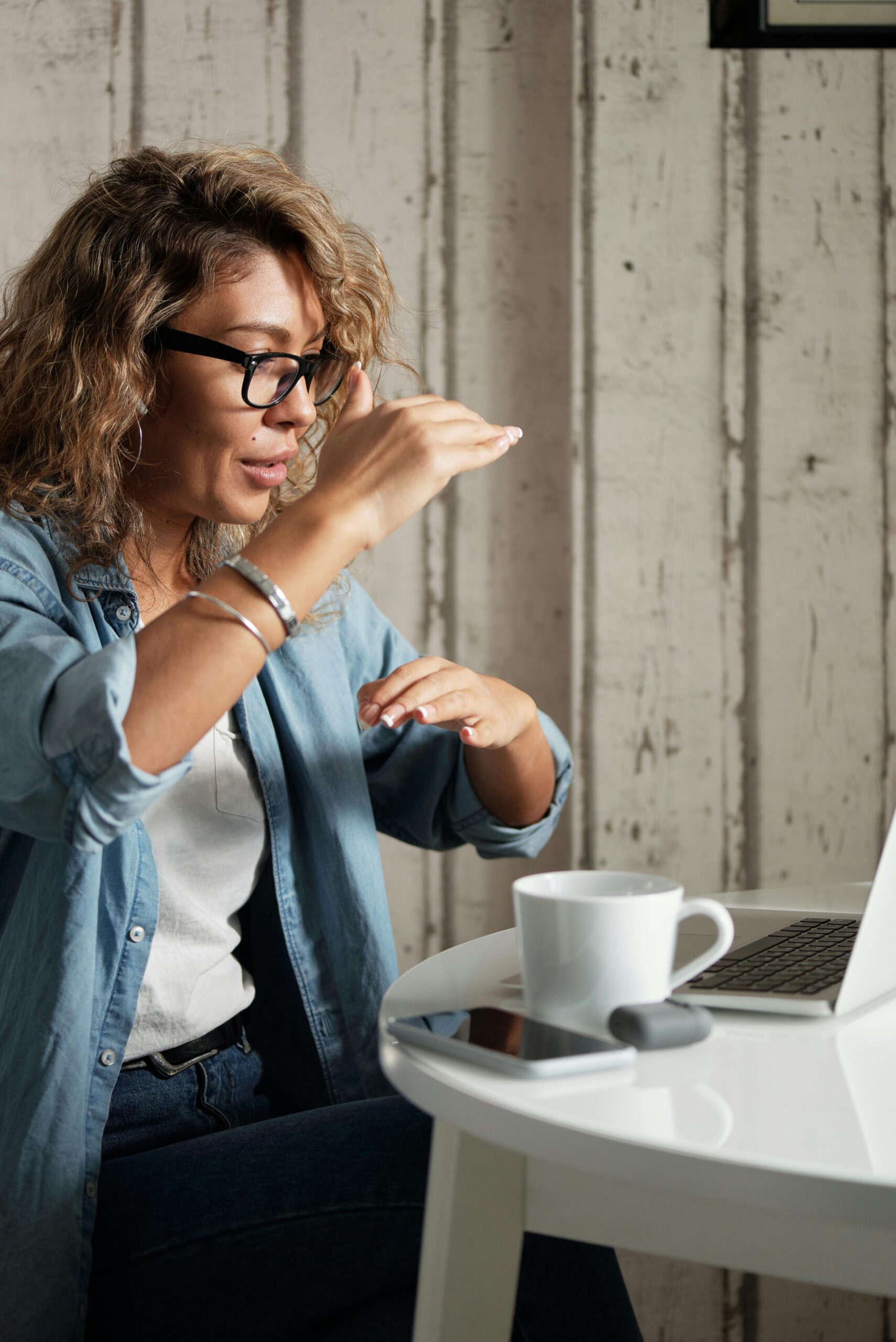 A young woman using gestures during a video conference at home, relaxed with a coffee.
